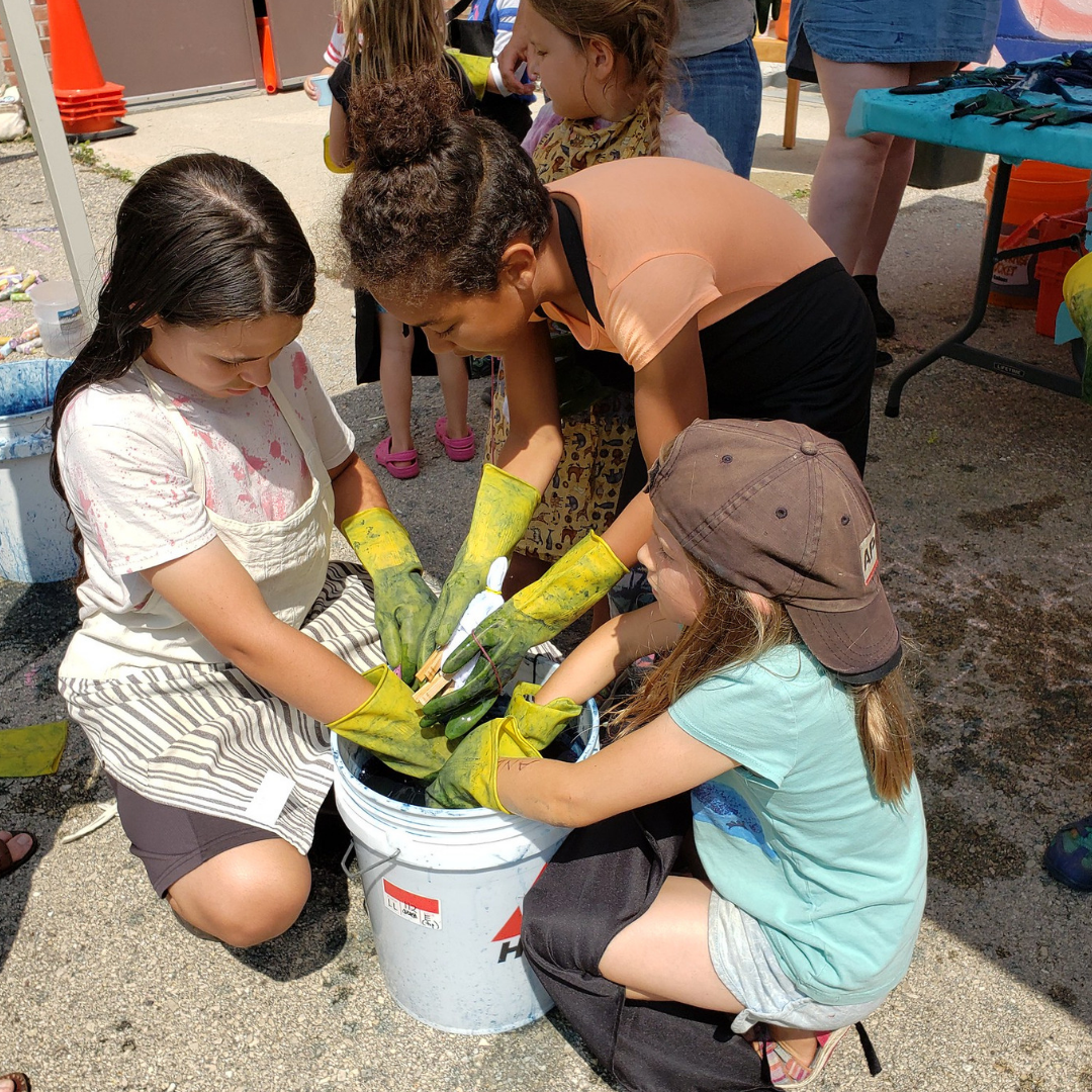 Kids reaching into a bucket of indigo dye during an Arts in the Alley event